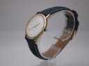 Angled side view of the Certina watch, showing the gold case, crown, and blue strap.