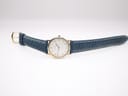 Full length view of the Certina watch with its blue leather strap and gold tone buckle, laid flat on a white surface.