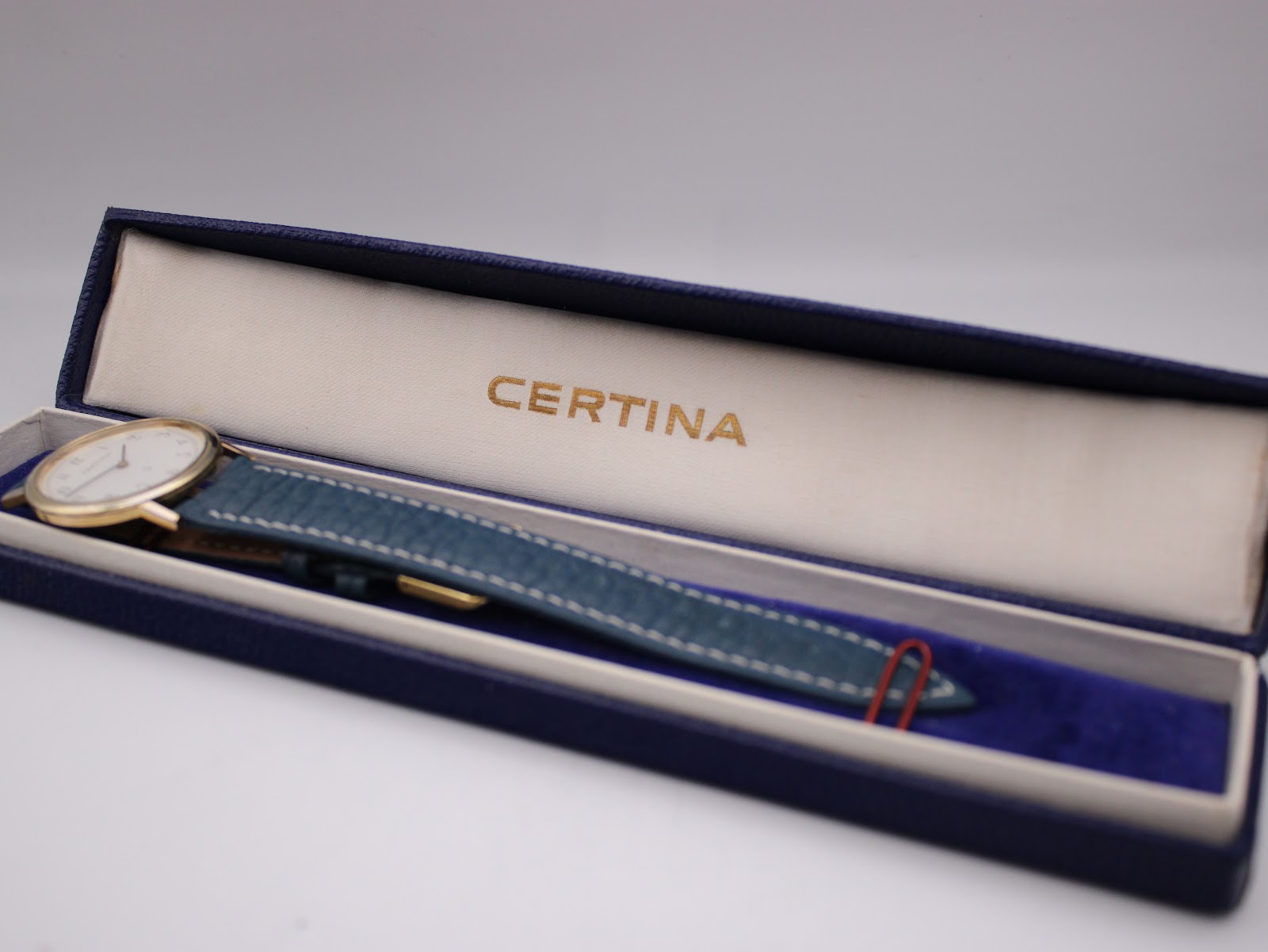 The Certina watch positioned inside its original dark blue presentation box with a gold 'CERTINA' logo.