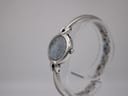 Side view of the Michel Herbelin watch on a clear stand, showing the case profile and integrated bangle bracelet.