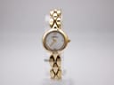 Front view of Michel Herbelin Paris ladies watch on a display stand, showing gold case and integrated bracelet, white mother of pearl dial with gold hands and XII Roman numeral.