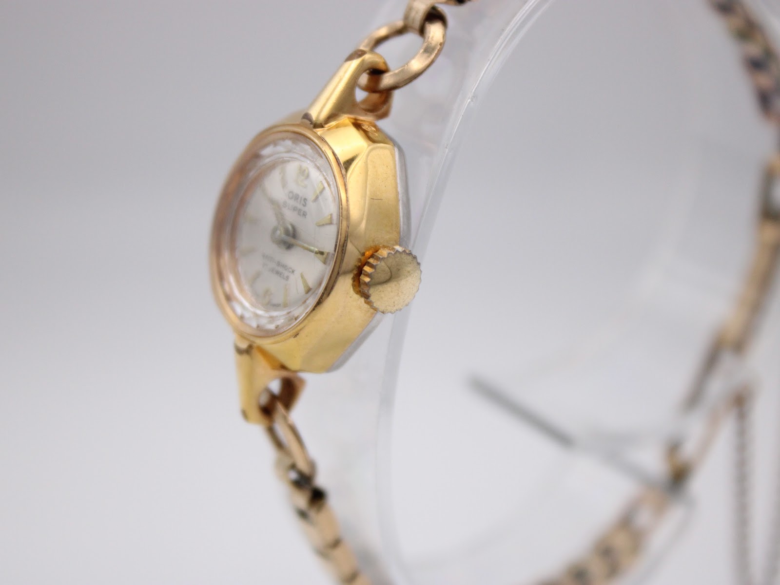 Side profile view of the gold Oris watch case and crown on a clear stand.