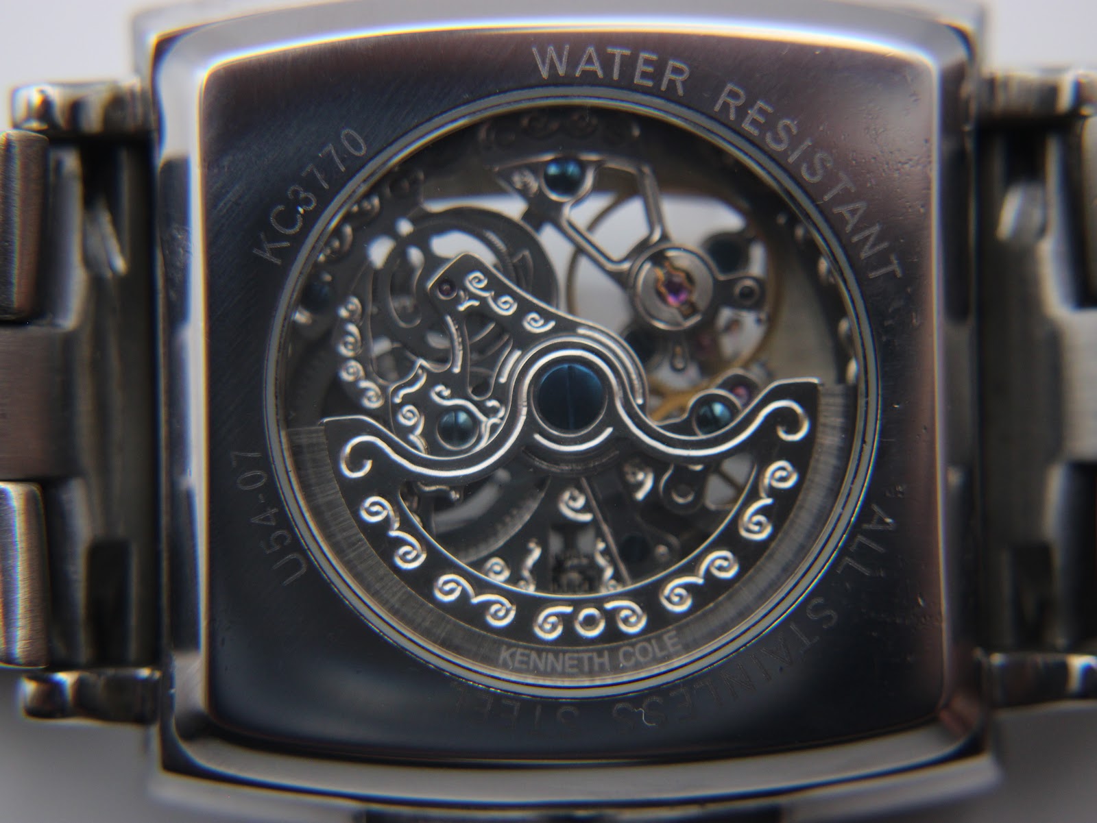 Close-up of the exhibition case back, revealing the intricate mechanical movement and 'WATER RESISTANT', 'ALL STAINLESS STEEL', 'KC3770', 'U54-07' engravings.