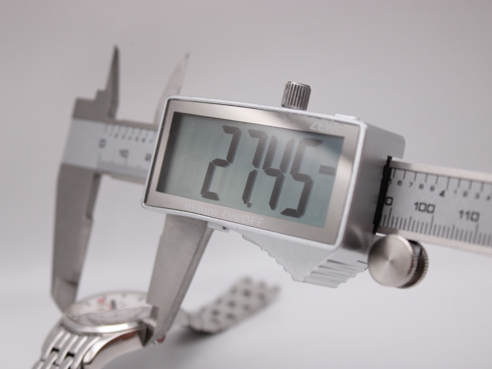 Digital caliper measuring the watch case diameter, with the display clearly showing a measurement of 27.5mm.