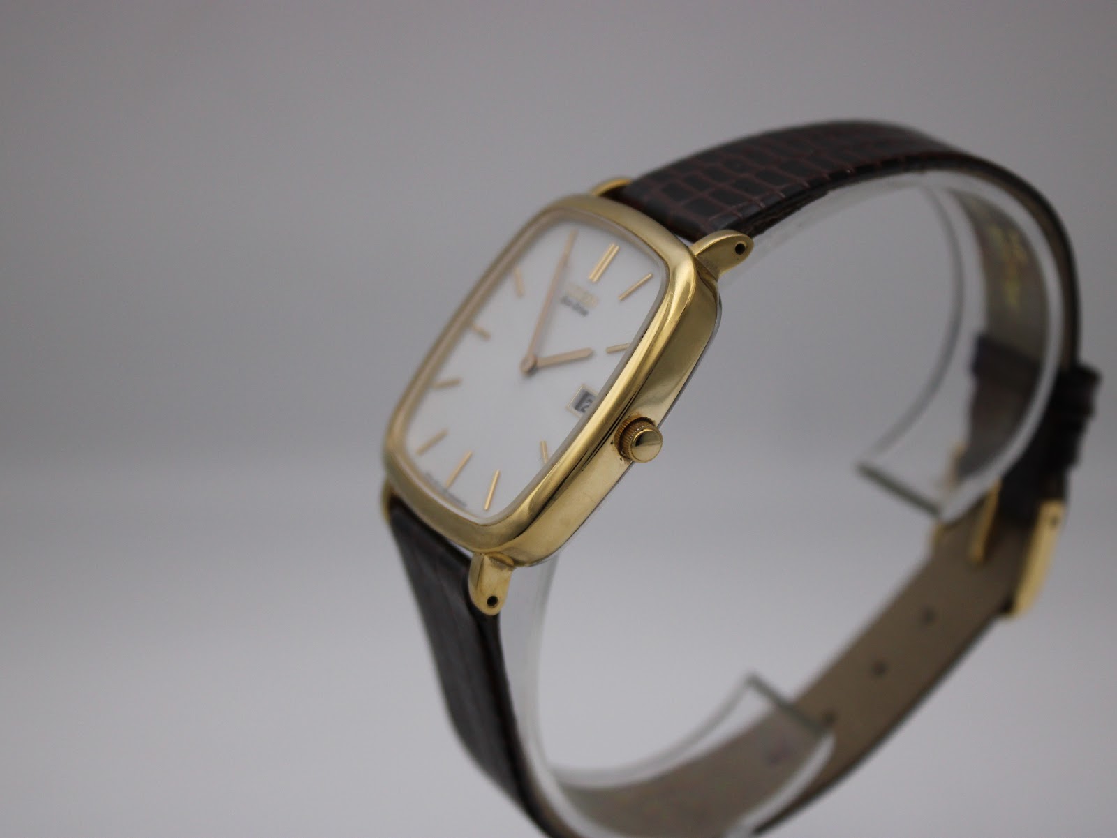 Angled side view of the gold-plated Citizen watch on a display stand, showing the crown.
