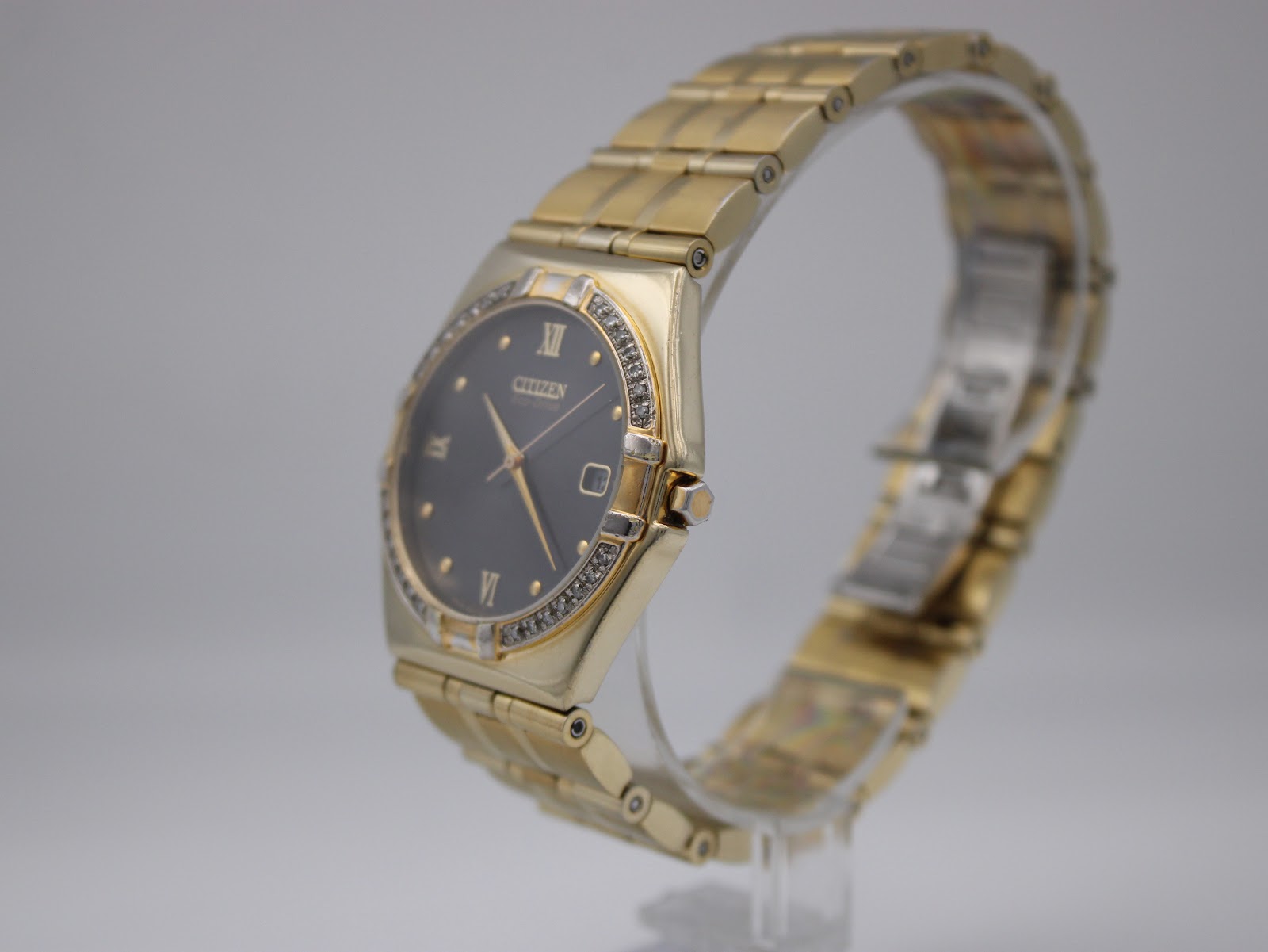Angled view of the gold-tone Citizen Eco-Drive watch on a display stand, highlighting the bracelet and tonneau case shape.