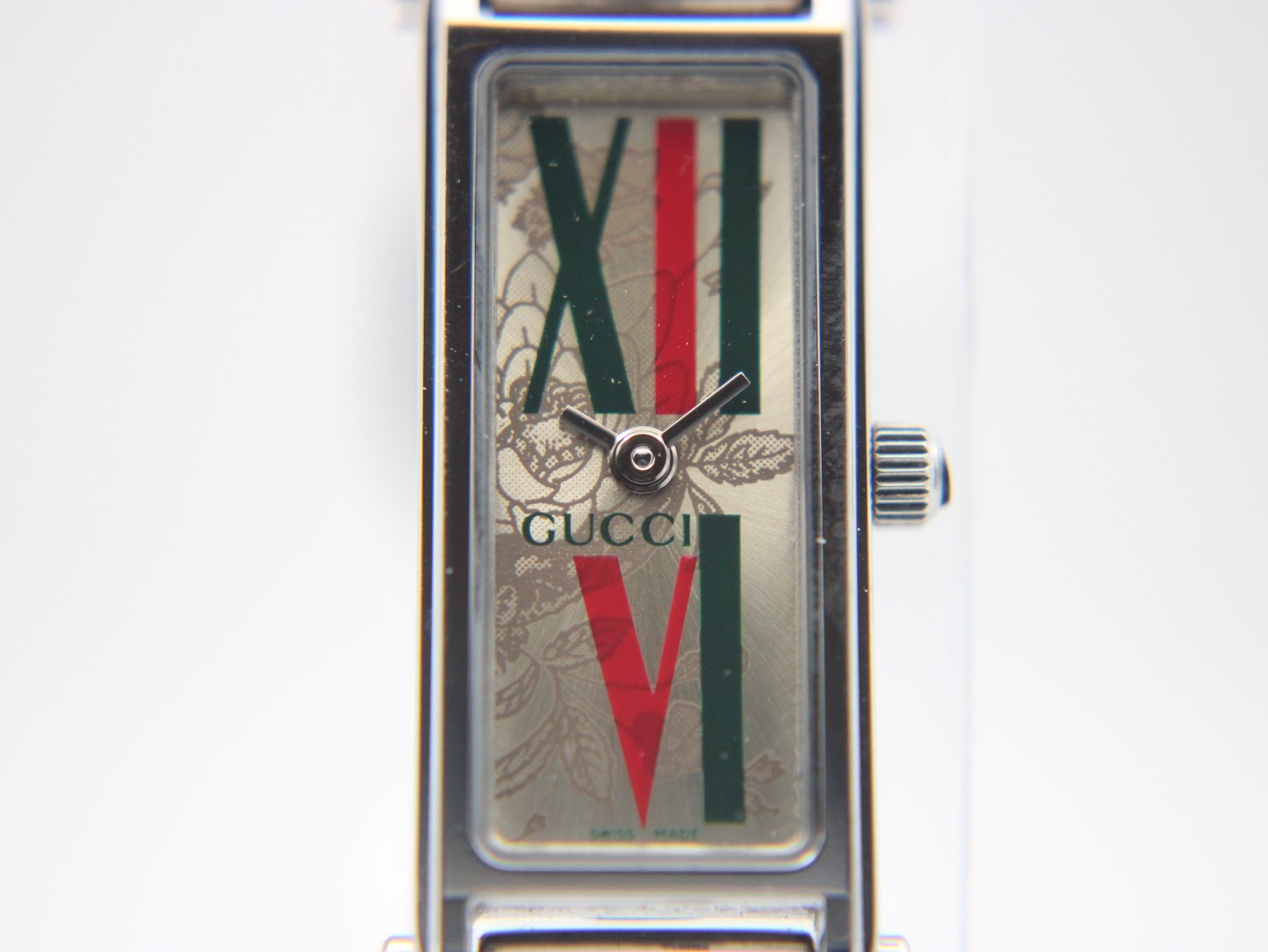 Close-up front view of the Gucci 1500L dial, clearly showing the green and red Roman numerals XII and VI, the Gucci logo, and the subtle floral background pattern.
