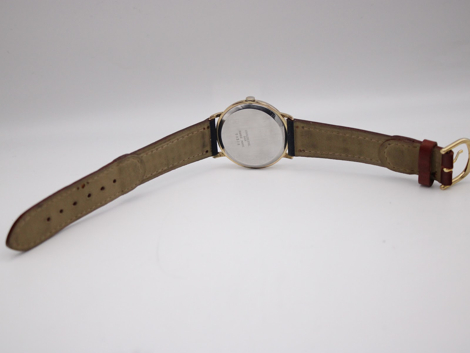 Rear view of the watch on a white background, showing the full length of the two-tone leather strap and gold-tone buckle.