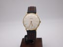 Front angled view of the gold plated Roamer watch on a display stand, showcasing its silver sunburst dial and two-tone perforated leather strap.