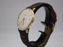 Side angled view of the gold plated Roamer watch on a stand, highlighting its slim case profile and domed acrylic crystal.