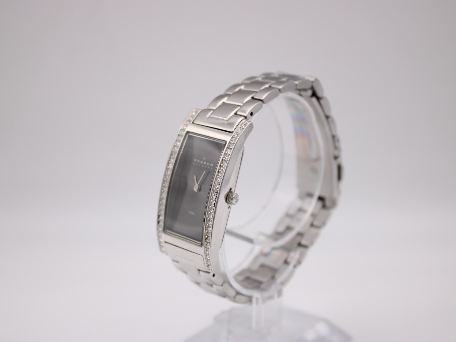 Angled view of the Skagen Denmark 459SSXM watch on a clear display stand, highlighting the curved case profile and integrated stainless steel bracelet.
