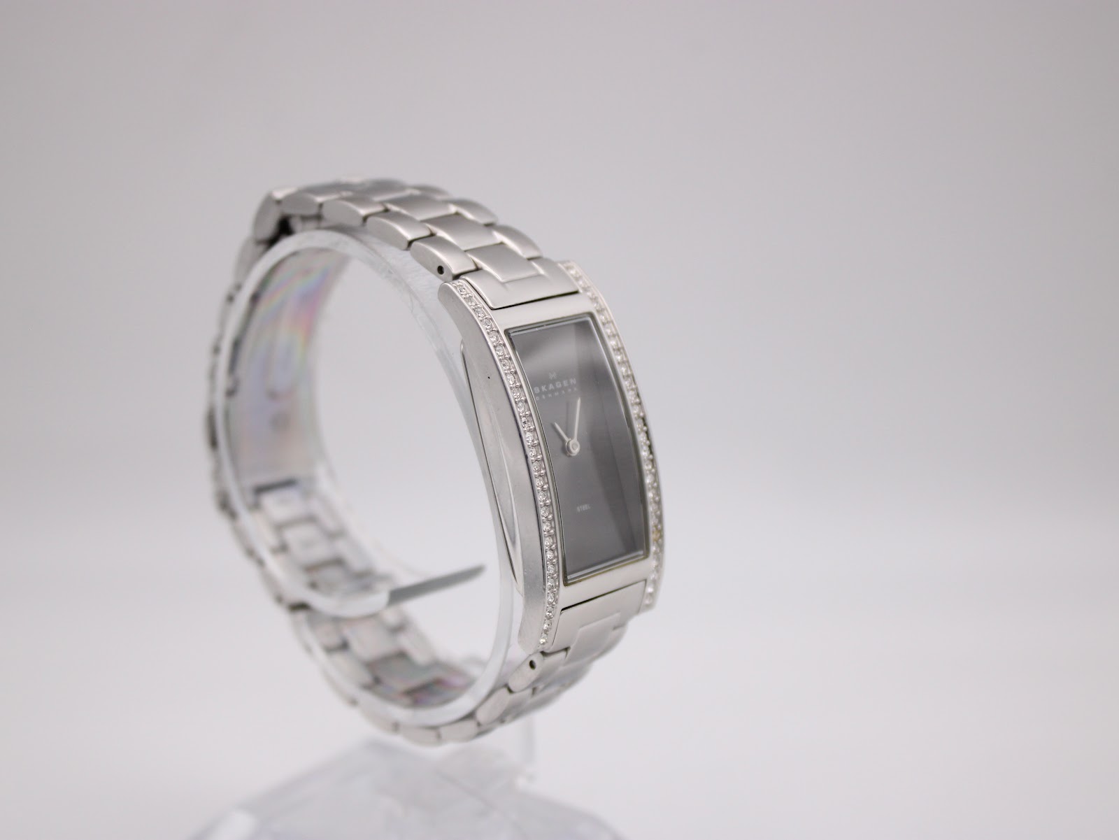 Side-on view of the Skagen Denmark 459SSXM watch on a clear display stand, showing the bracelet's curve and the crystal embellishments along the case.