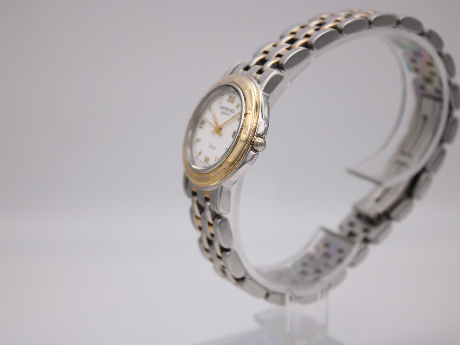 Angled side view of the Raymond Weil Tango watch on a clear display stand, highlighting its profile.