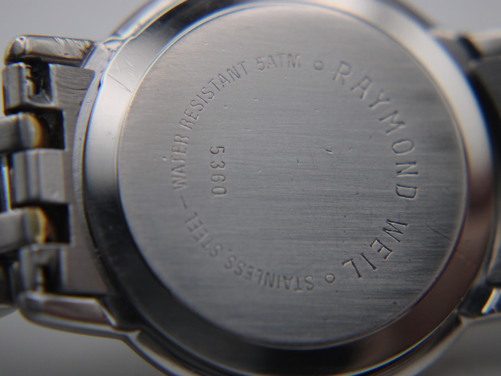 Close-up of the stainless steel case back, engraved with 'Water Resistant 5ATM', 'Stainless Steel', '5360', and 'Raymond Weil'.