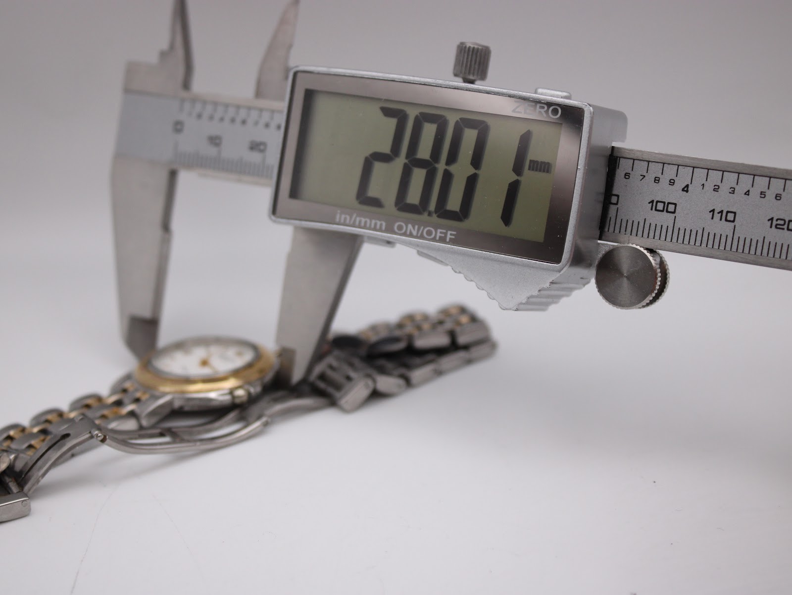 A digital caliper measuring the watch case diameter, displaying an exact measurement of 28.01mm.