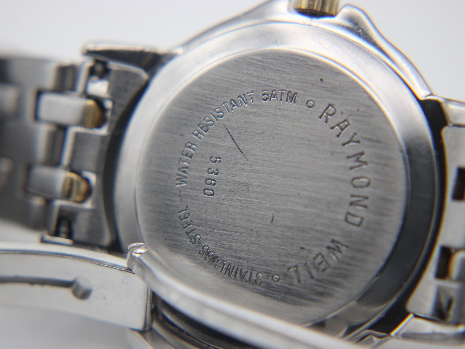 Close-up of the watch case back, showing 'Raymond Weil', 'Stainless Steel', '5360', and 'Water Resistant 5ATM' engravings.