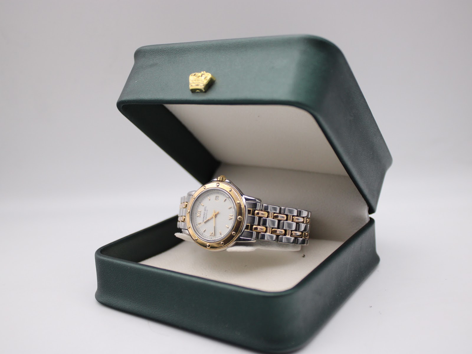 Raymond Weil Tango watch resting inside an open dark green presentation box.