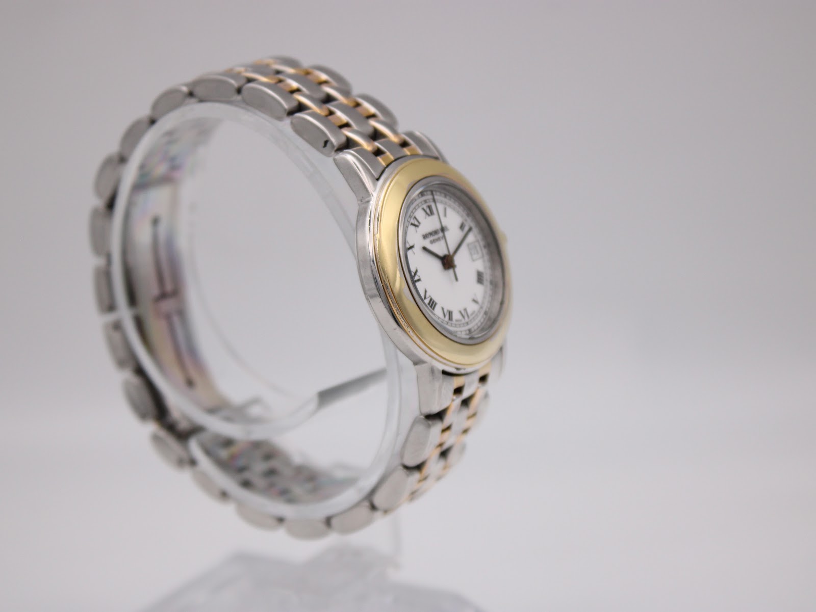 Opposite angled side view of the Raymond Weil watch, highlighting the gold-tone bezel and bracelet links.