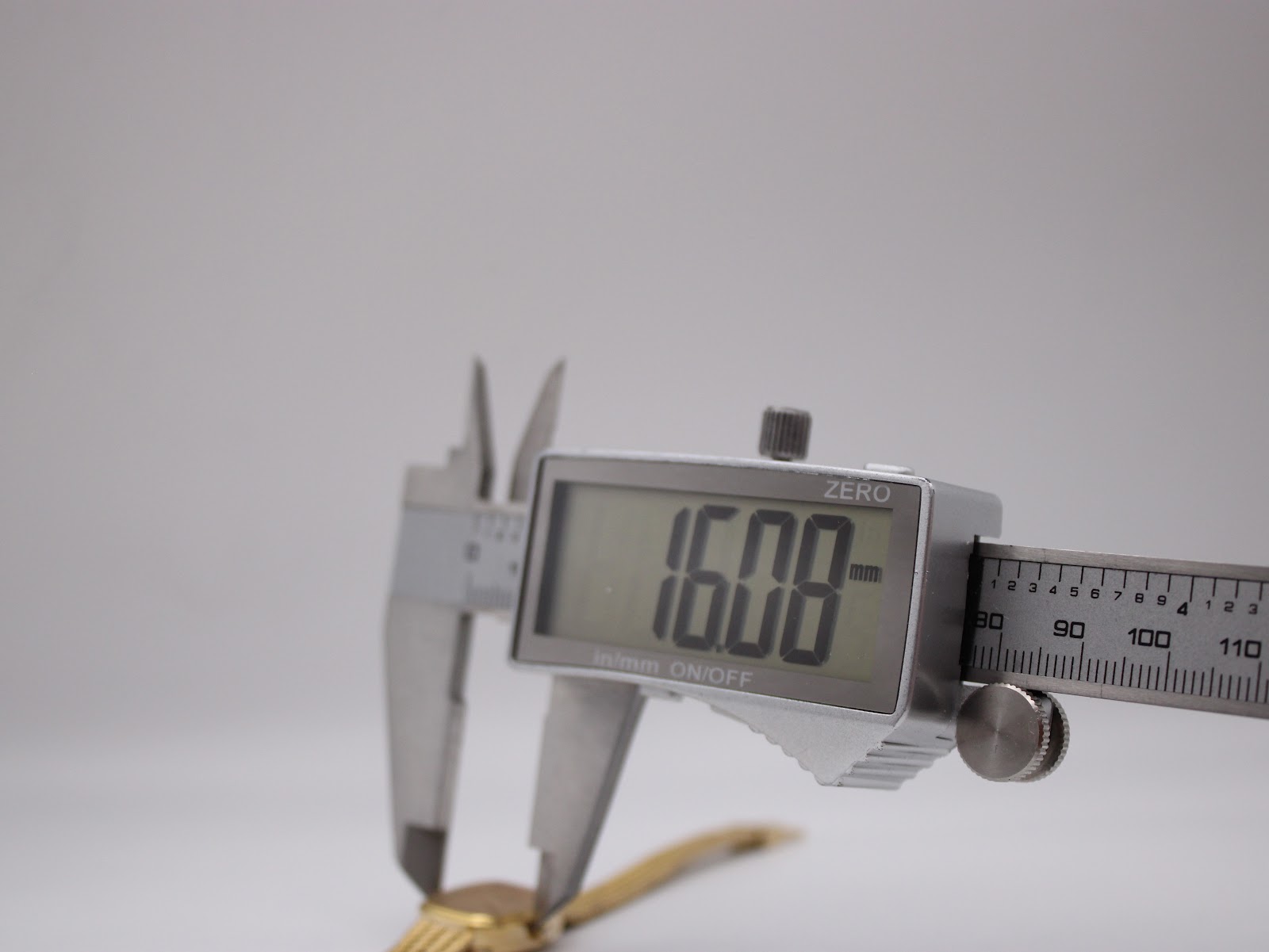 Close-up of a digital caliper measuring the watch case, displaying a precise reading of 16.08 mm.