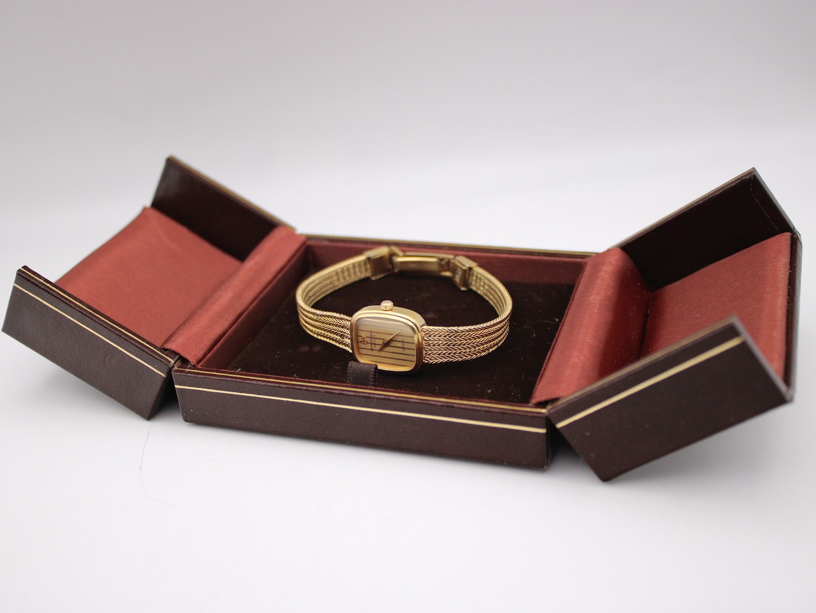 The Raymond Weil watch nestled within an open brown hinged watch box with a velvet interior.