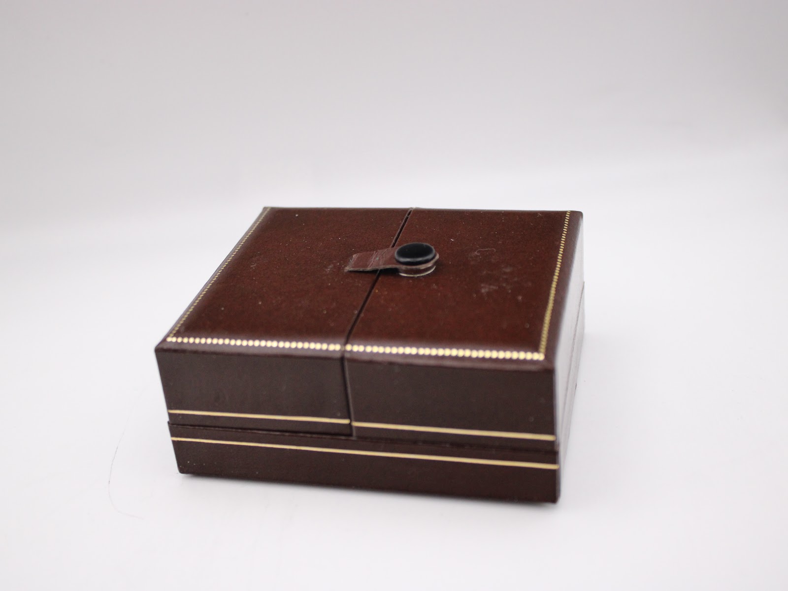 A closed view of the vintage brown watch box with gold trim, featuring a central strap clasp.