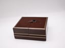 A closed view of the vintage brown watch box with gold trim, featuring a central strap clasp.