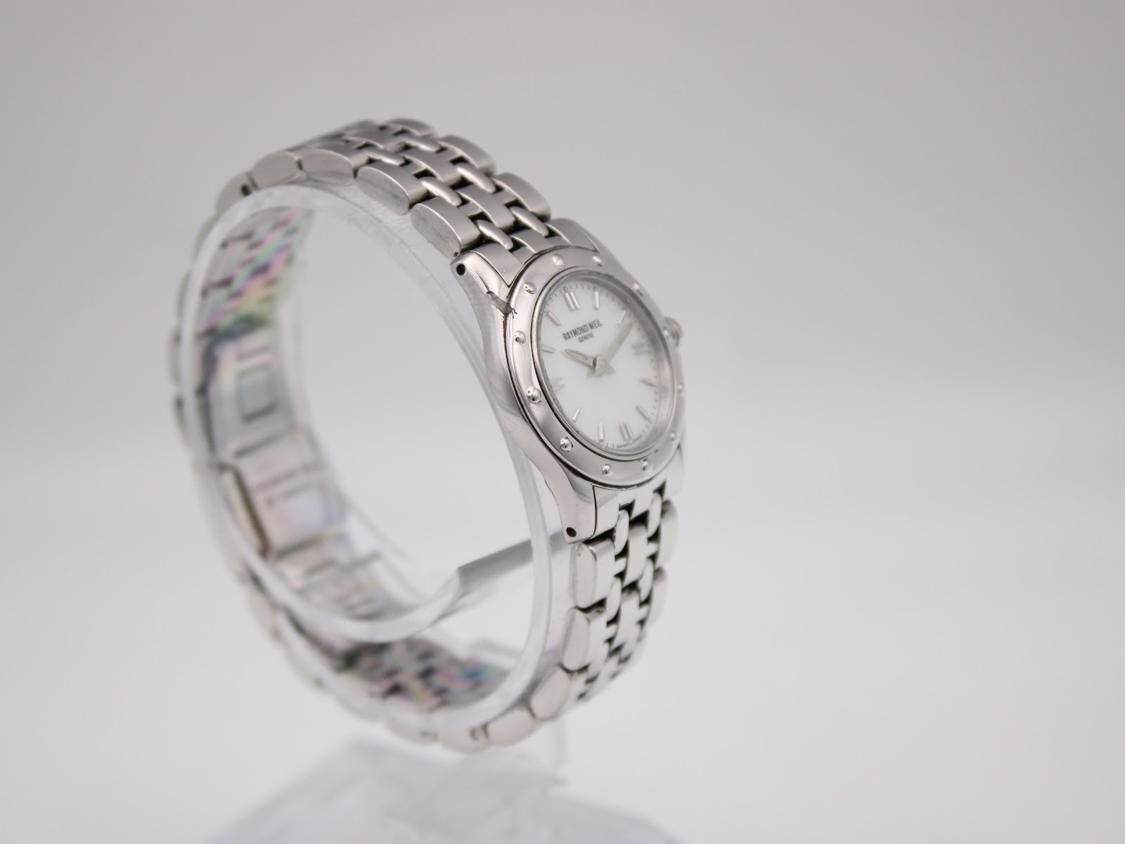 Left side angle view of Raymond Weil Tango watch on a clear stand, highlighting the bracelet links and case curves.