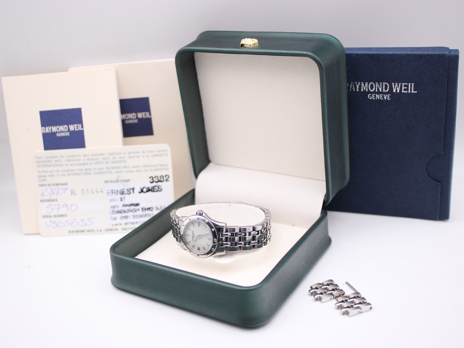 Raymond Weil Tango watch nestled in a dark green presentation box, with its instruction papers, guarantee card, and extra bracelet links visible.