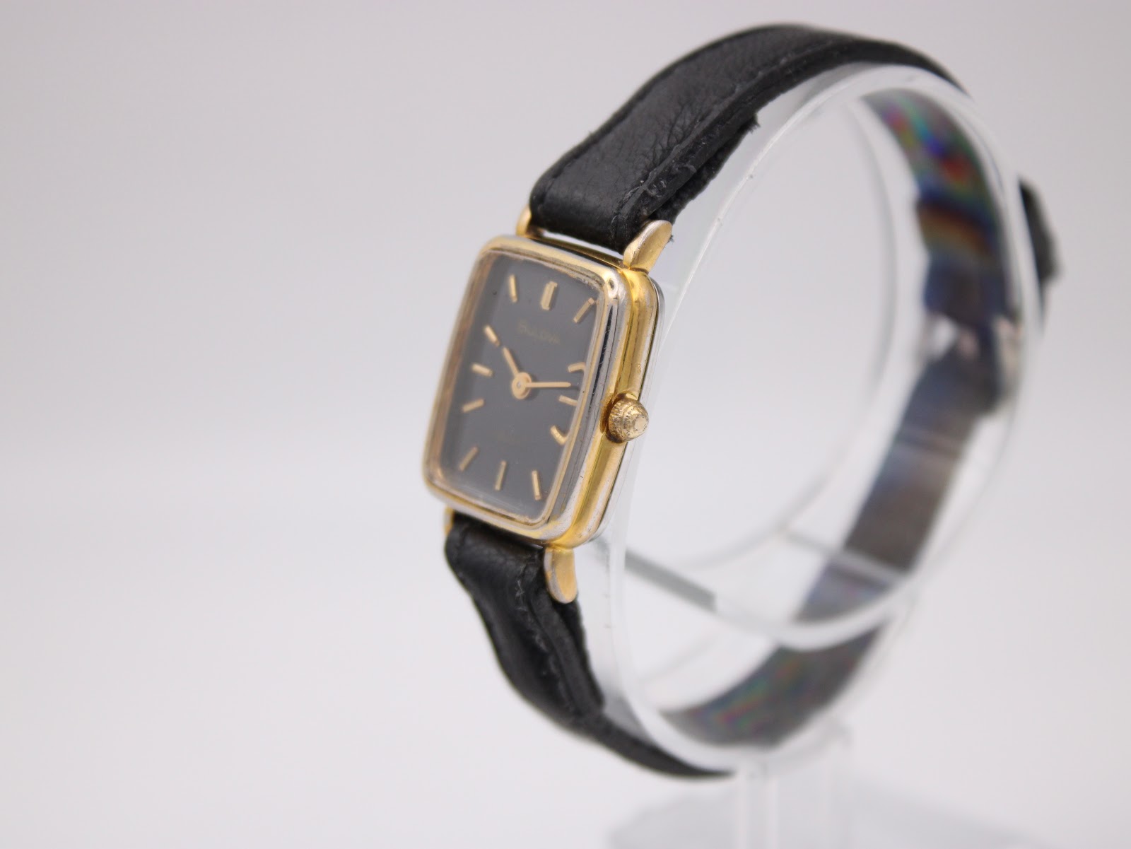 Angled side view of the Bulova SL200 watch on a stand, highlighting the gold tone rectangular case and signed crown.