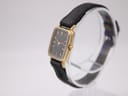 Angled side view of the Bulova SL200 watch on a stand, highlighting the gold tone rectangular case and signed crown.