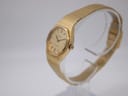 Angled view of the gold Tissot Stylist showing the crown and integrated bracelet on a clear stand.