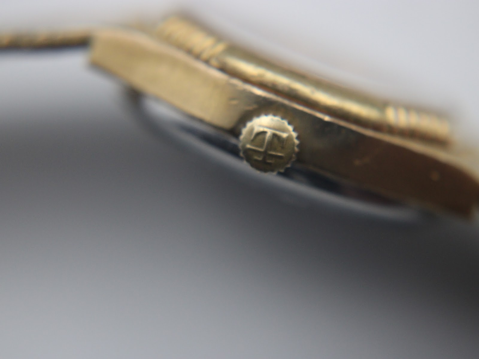 Macro shot of the original Tissot signed crown with the brand's 'T' logo.