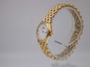 Oblique side view of the gold Raymond Weil watch and bracelet on a clear display stand, highlighting the crown.