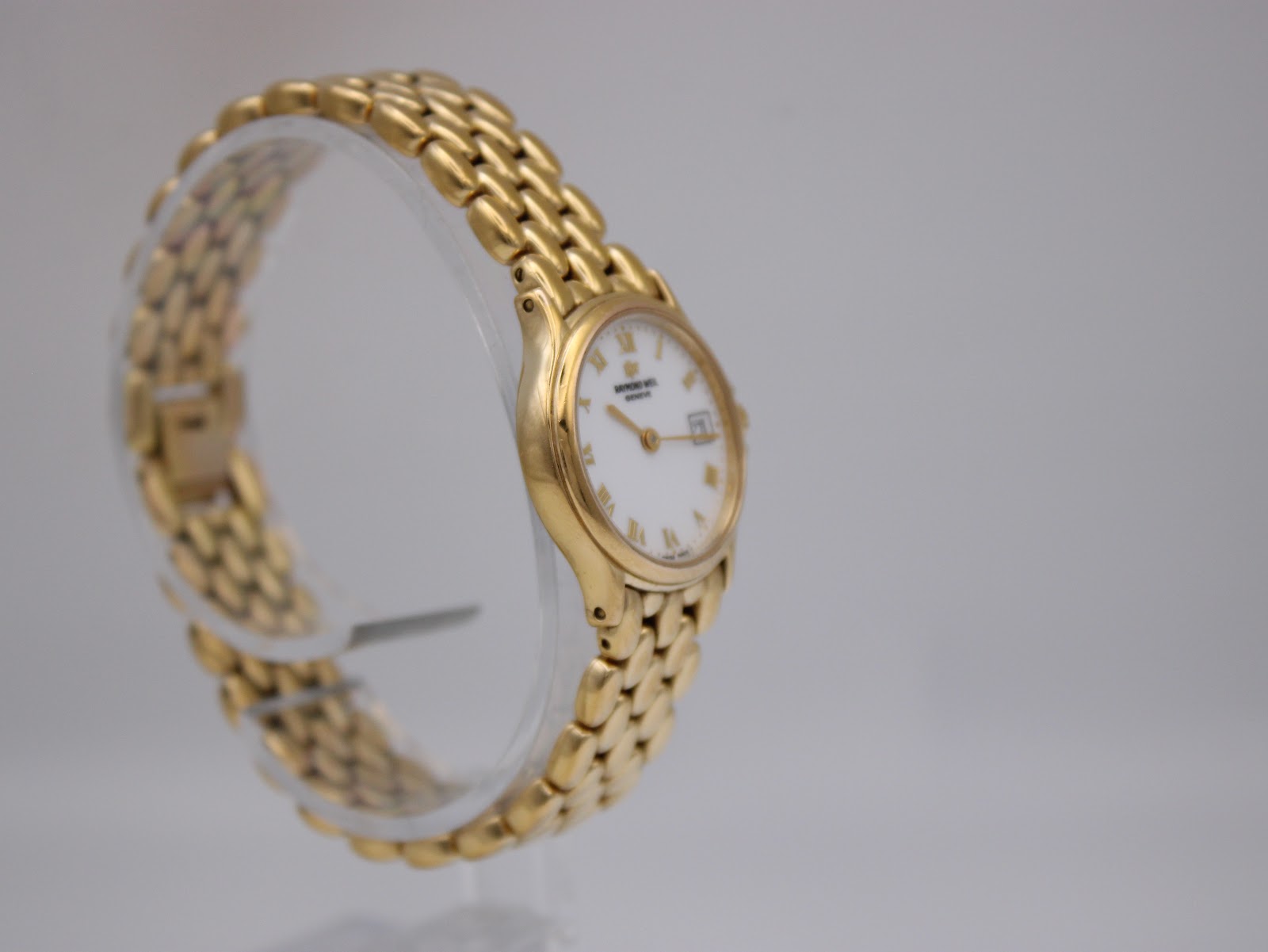 Another oblique side view of the gold Raymond Weil watch and its 'rice bead' style bracelet on a clear display stand.