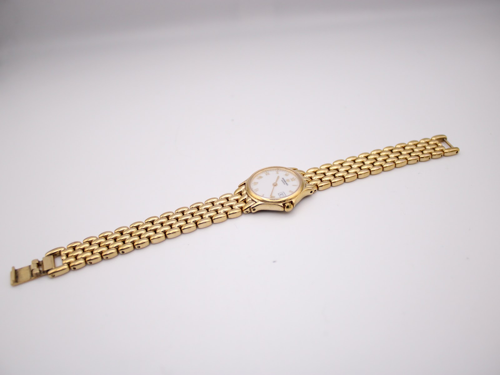 Full length view of the gold Raymond Weil watch and 'rice bead' bracelet laid flat, showing the front of the watch.