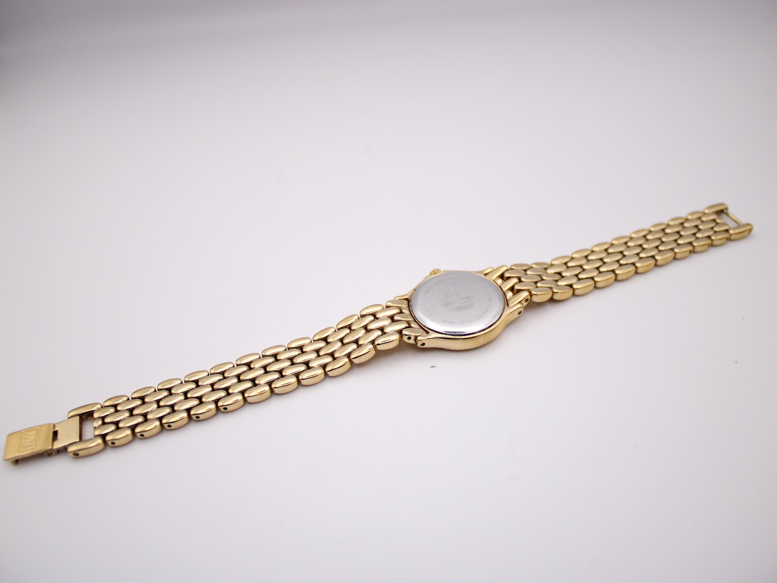 Full length view of the gold Raymond Weil watch and bracelet laid flat, showing the case back.