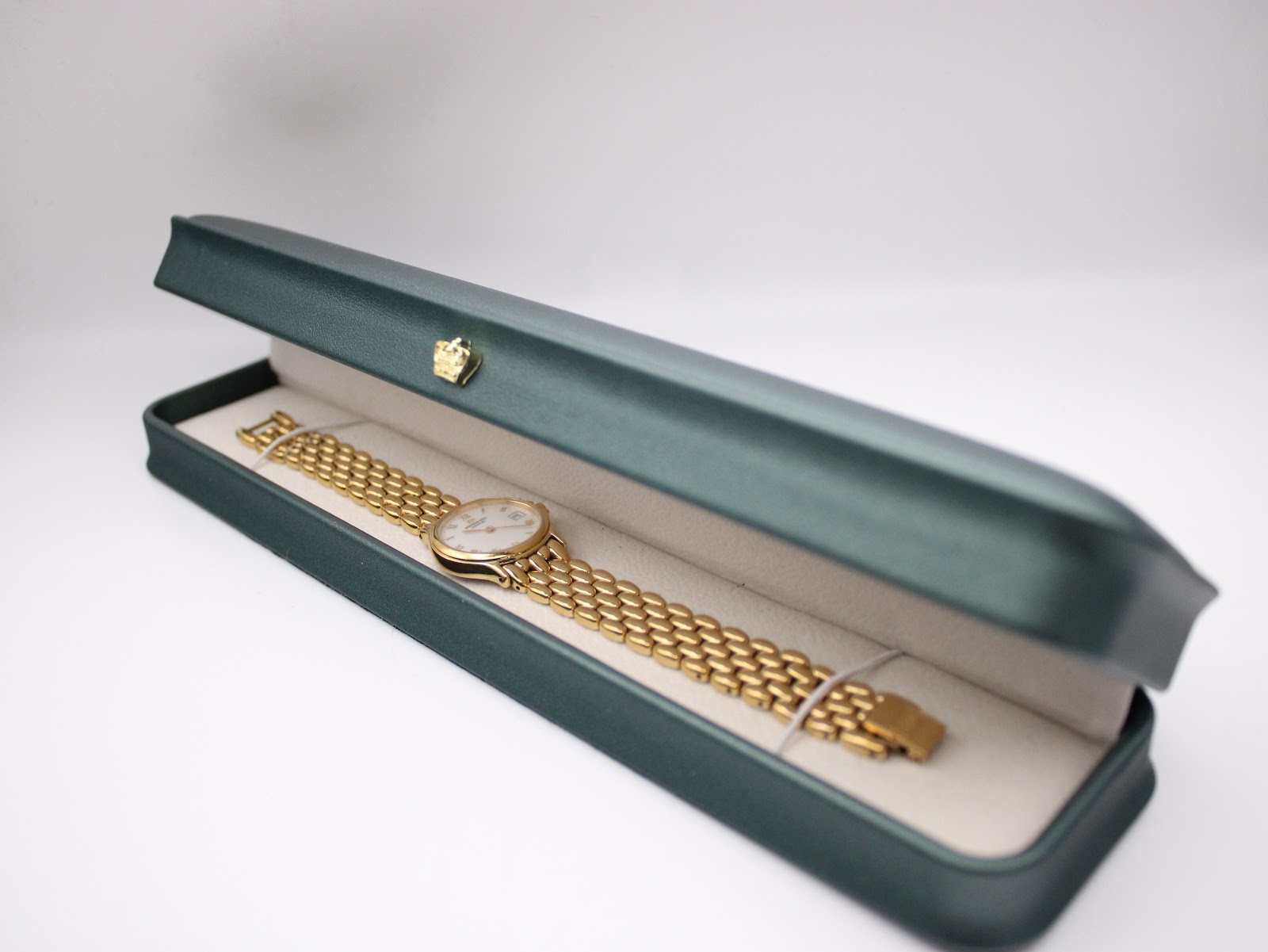 The gold Raymond Weil watch and bracelet resting inside an opened dark green presentation box with a cream interior.