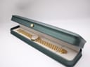 The gold Raymond Weil watch and bracelet resting inside an opened dark green presentation box with a cream interior.
