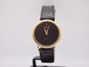 Front view of a gold Raymond Weil watch with black wave pattern dial and diamond at 12 o'clock, on a black leather strap.