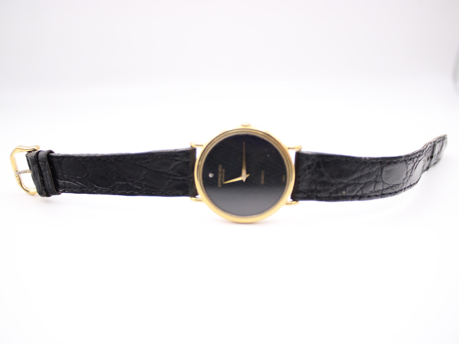 Full frontal view of the Raymond Weil watch unbuckled, lying flat, showcasing the gold case, black dial, and black leather strap.
