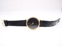 Full frontal view of the Raymond Weil watch unbuckled, lying flat, showcasing the gold case, black dial, and black leather strap.