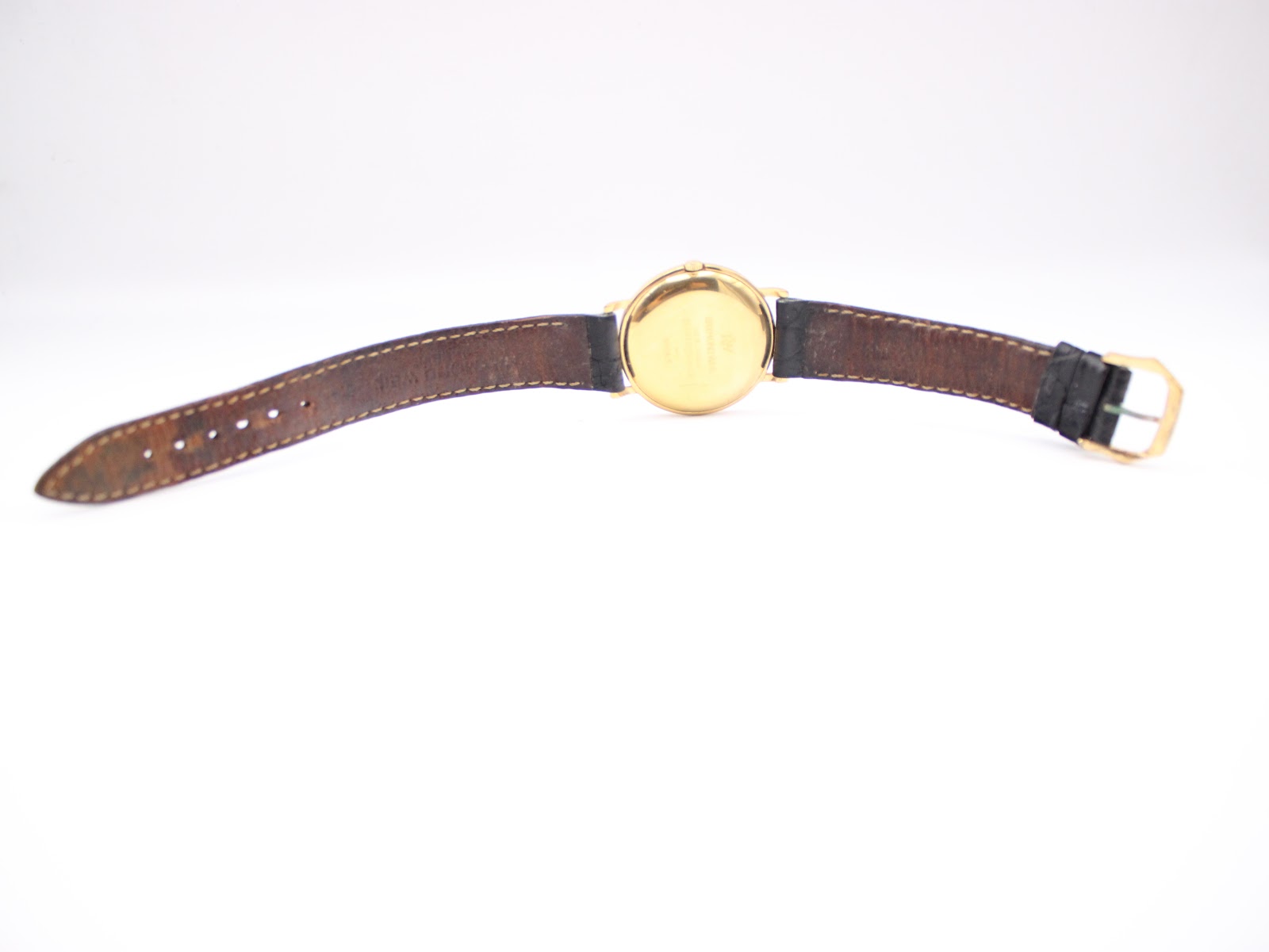 Back view of the Raymond Weil watch unbuckled, lying flat, revealing the underside of the black leather strap and the gold case back.