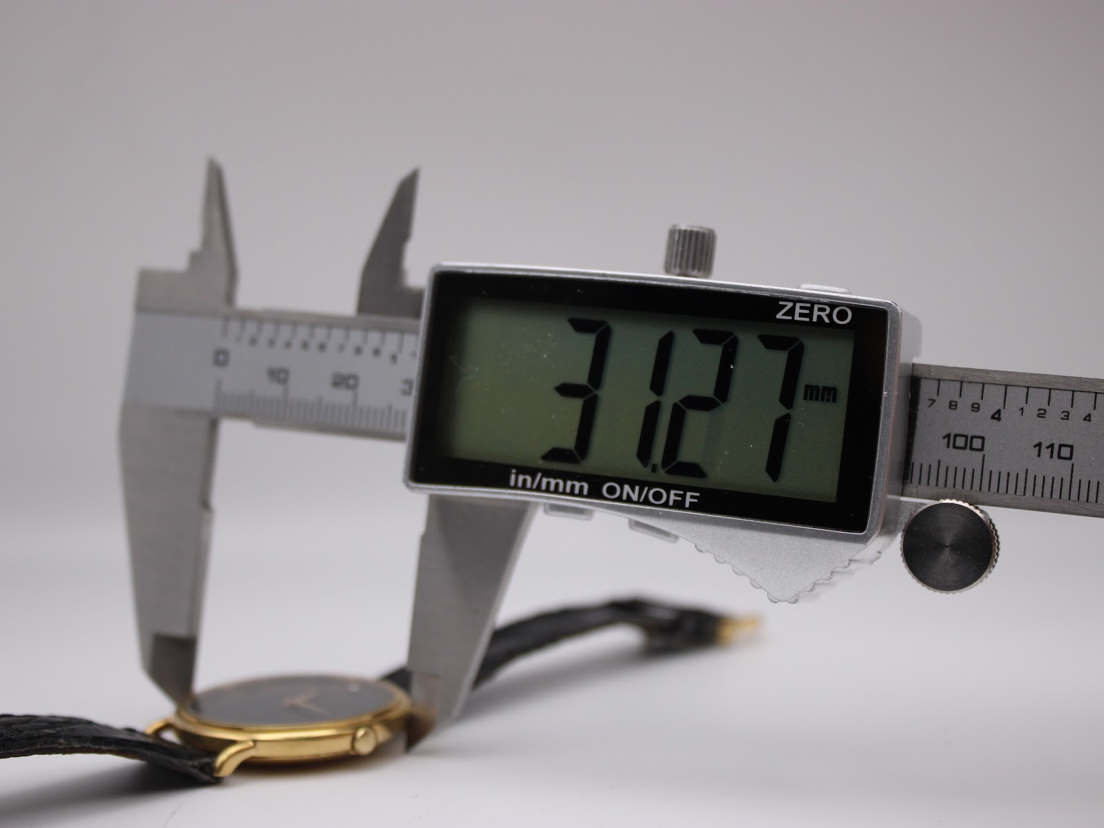 Digital caliper measuring the watch case, with the display clearly showing '31.27 mm'.