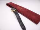 The Raymond Weil watch with its black strap partially placed inside its original red velvet pouch.
