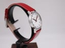 Another angled view of the Mondaine watch on a stand, highlighting the case profile and red strap.