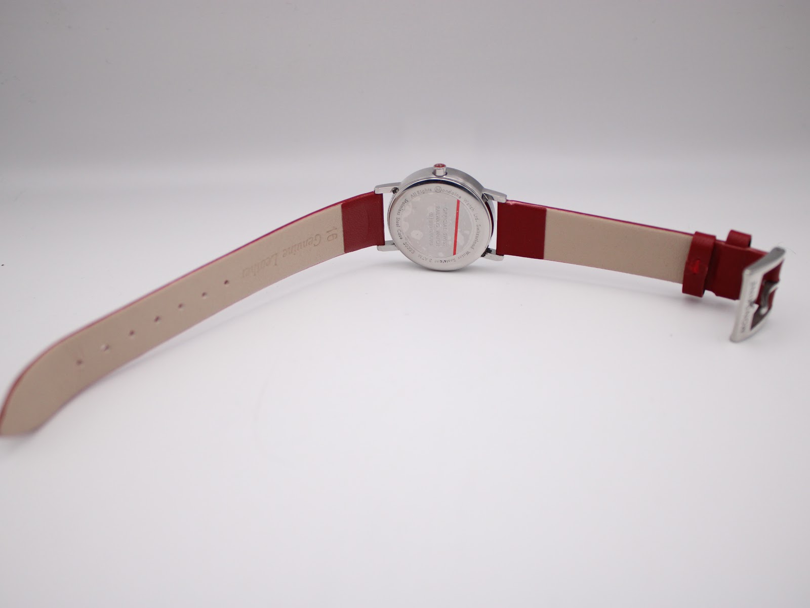 Back view of the Mondaine watch with the red leather strap unbuckled, showing the case back and strap lining.