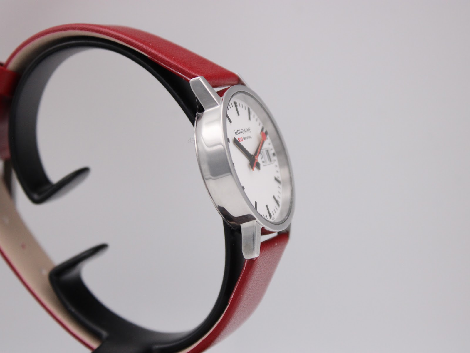 Three-quarter view of the Mondaine watch, showing the dial, case profile, and strap from a slight angle.