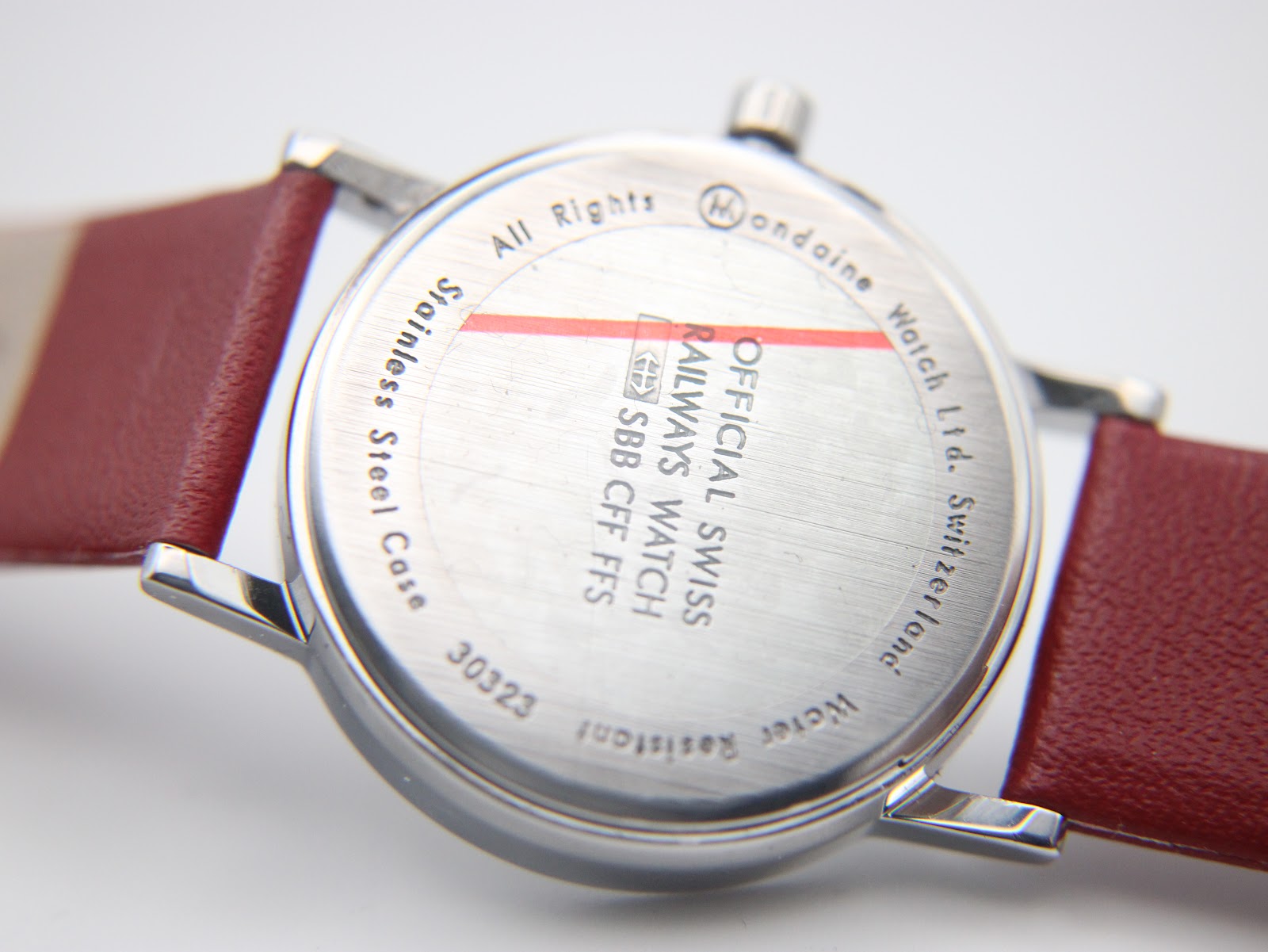 Close-up of the stainless steel case back of the Mondaine watch, showing engraved text including "Official Swiss Railways Watch", "SBB CFF FFS", "Stainless Steel Case", "30323", and "Water Resistant".