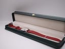 Mondaine watch with red strap presented inside a dark green, cream-lined watch box, ready for presentation.