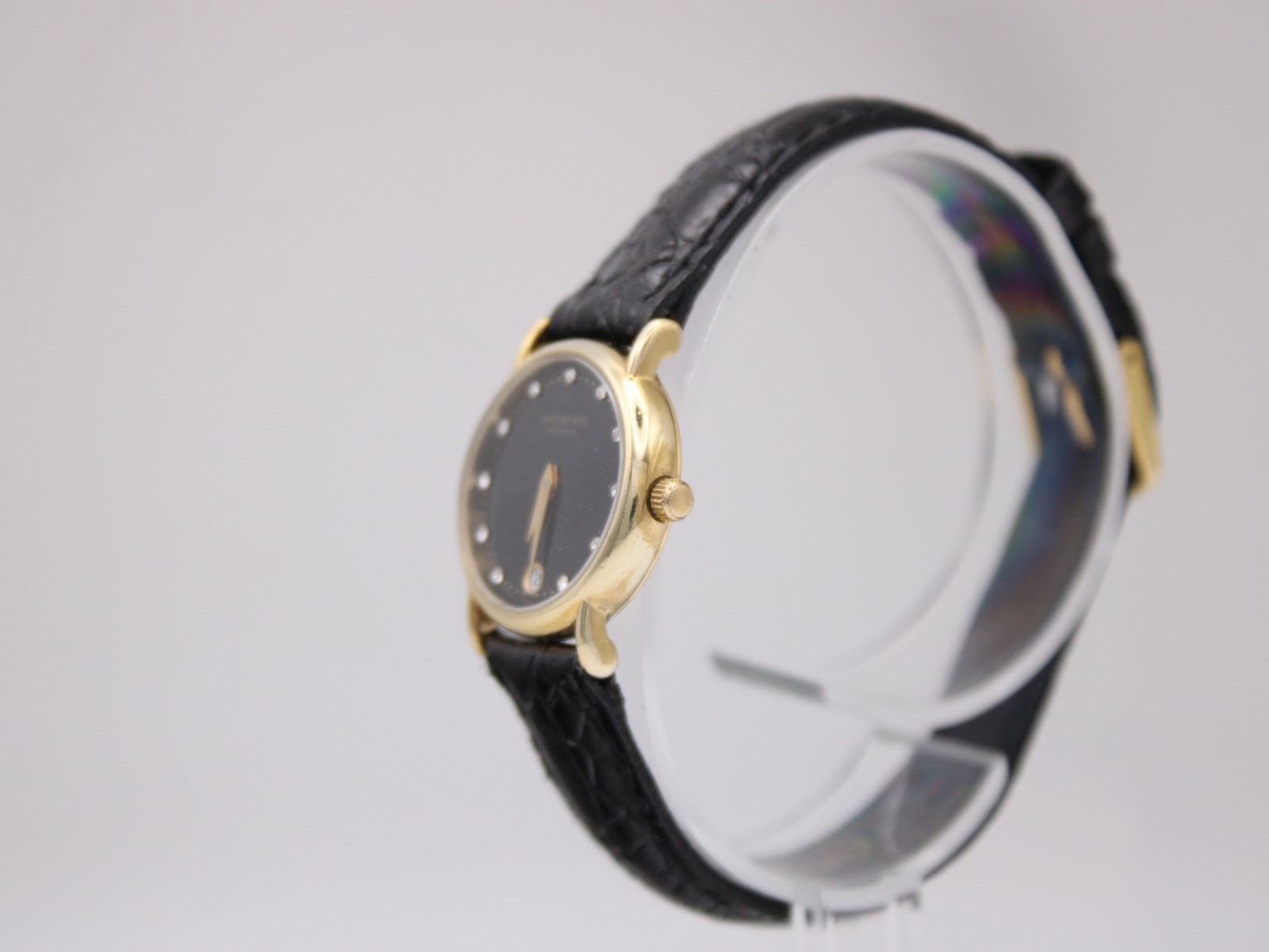 Angled side view of the Raymond Weil watch from the right, showing the gold-tone crown and the profile of the round case and black leather strap.